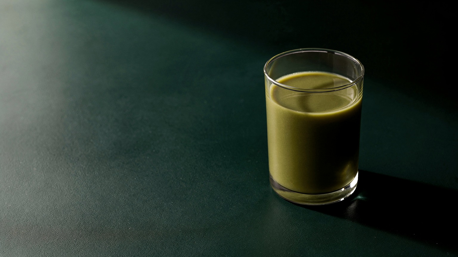 Generated concept image of a single green drink on a dark green surface with restrained lighting.