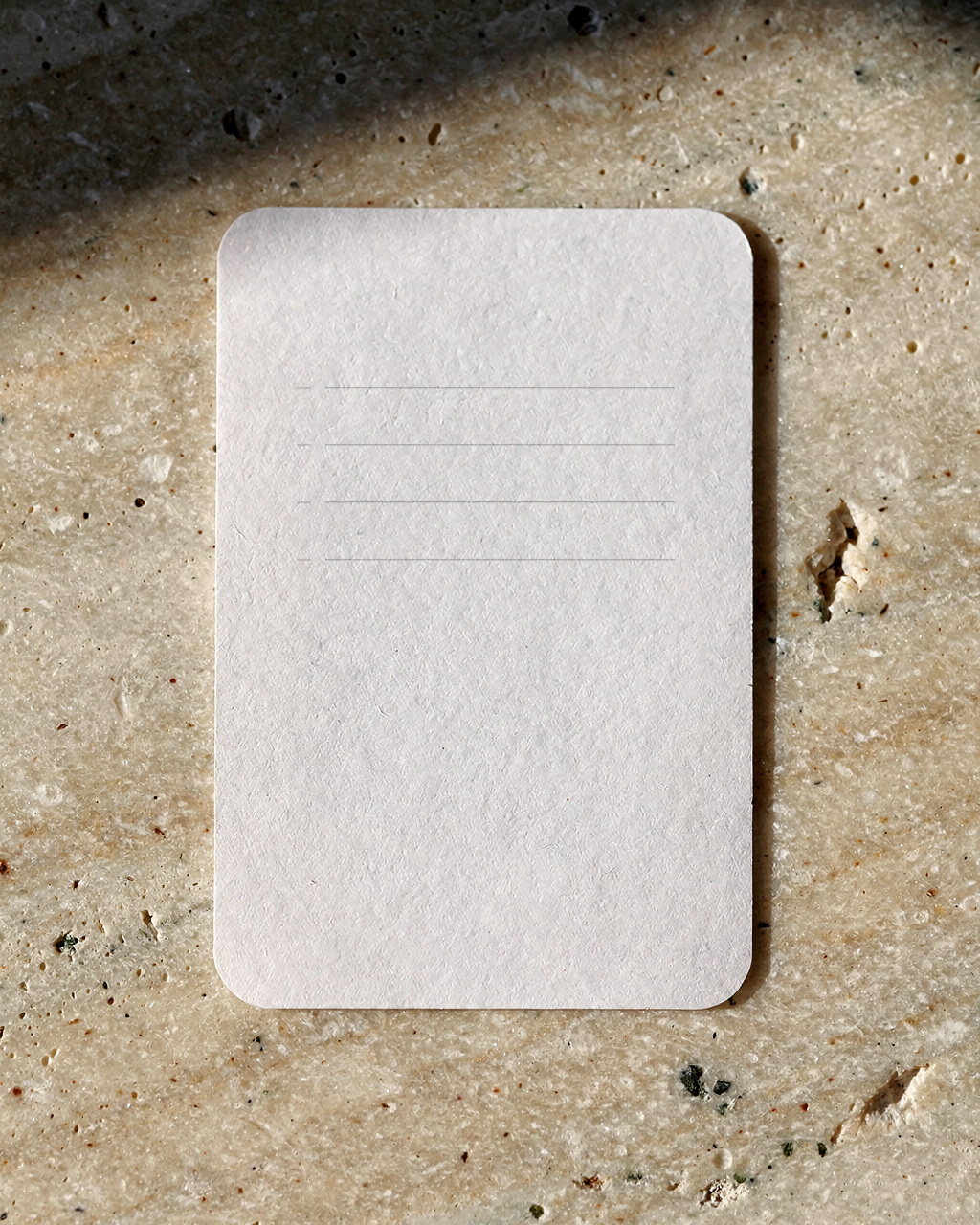 Generated concept image of a small blank cream card with evenly spaced ruled lines on stone.