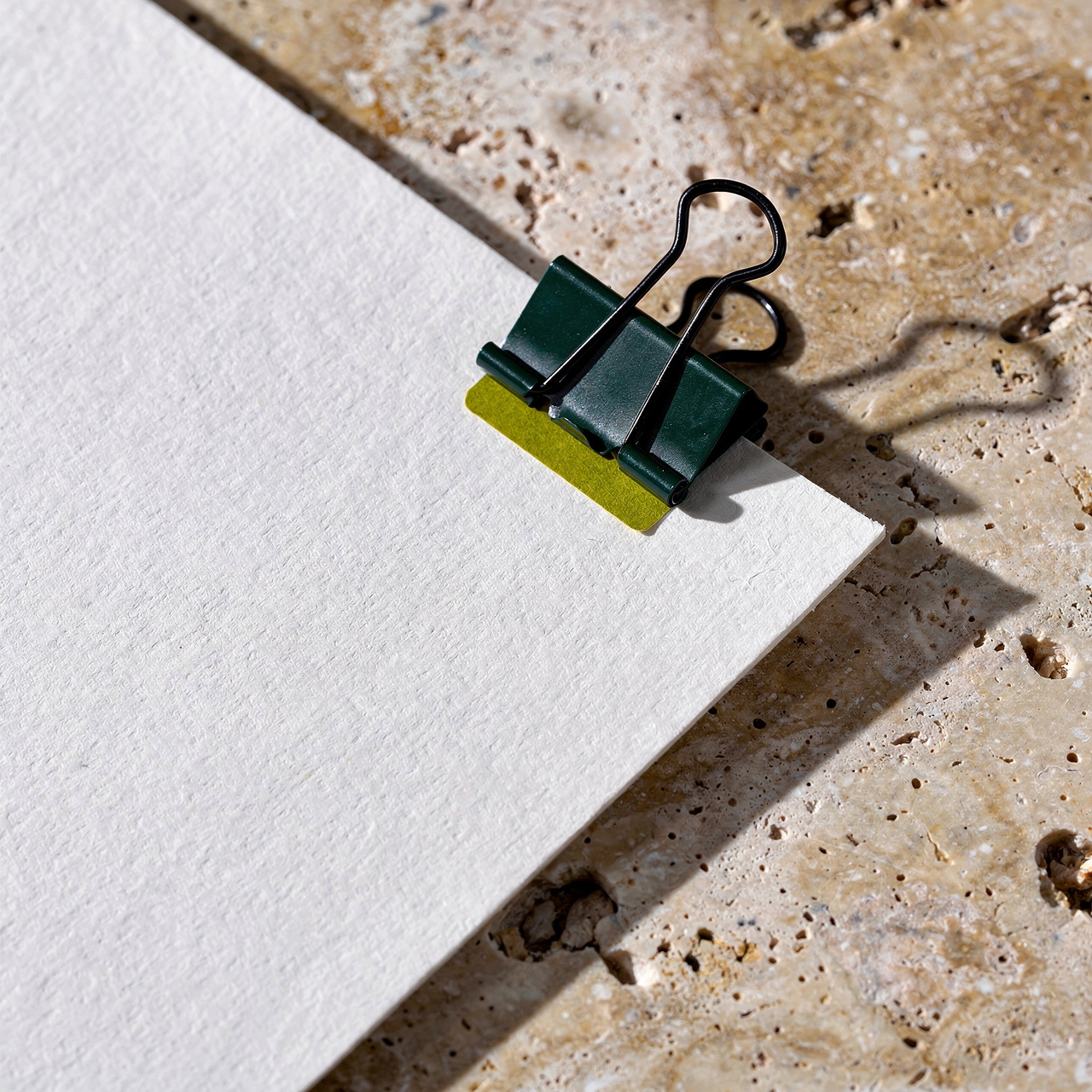 Generated concept image of cream paper clipped with a dark green binder clip on stone.